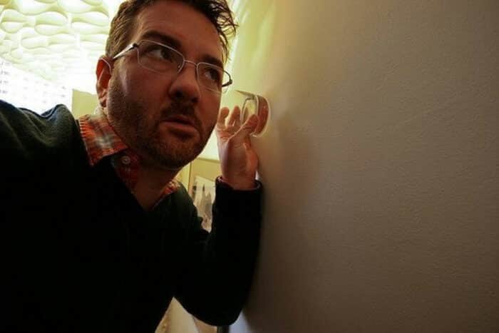 man uses a glass cup to listen in on a wall