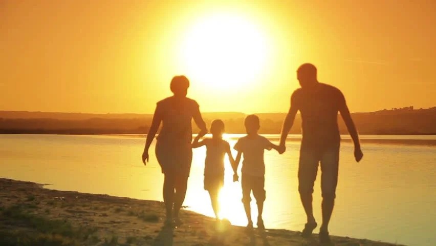 Padres con sus hijos caminando a la orilla de la playa en un atardecer