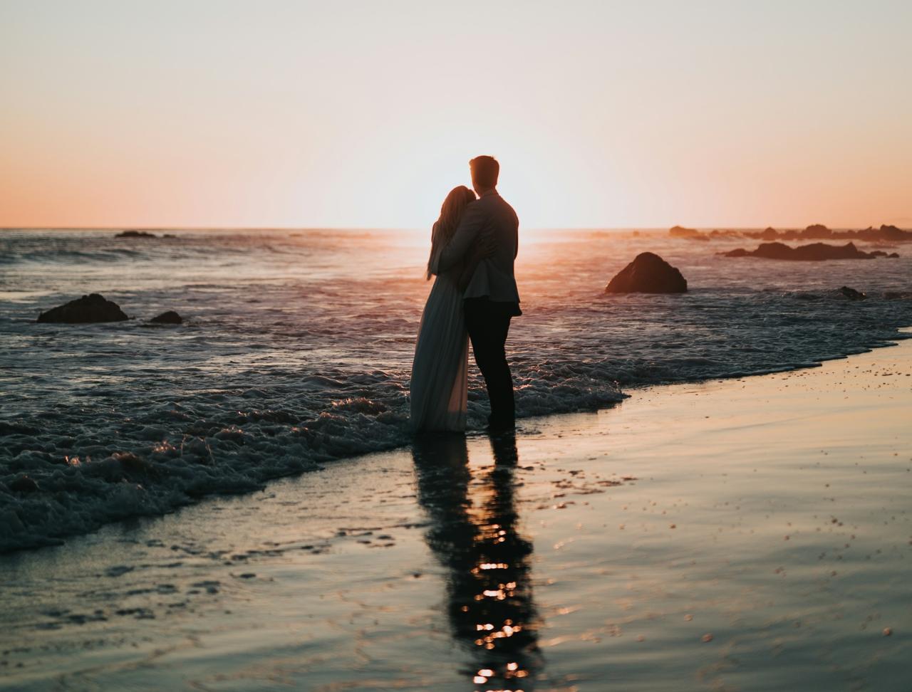 silhouette photo of a couple standing on the beach watching the sunset